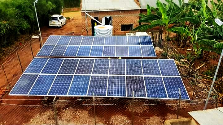 Two rows of solar panels inside a wire fence beside a building